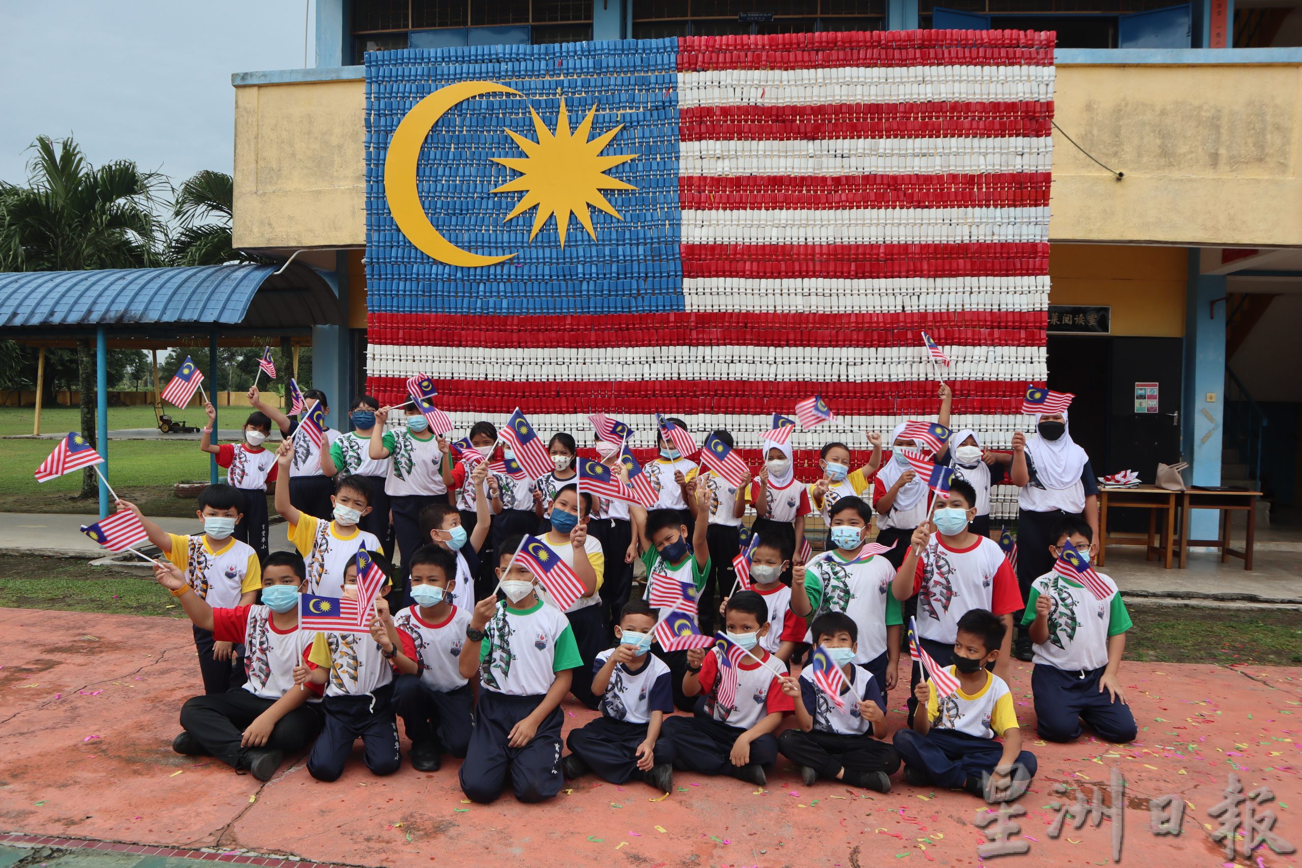 关丹育贤华小约300名师生，使用近千个塑料益生菌瓶子，费时两周，制作出10公尺乘14公尺的巨型国旗，让学生感受绿色国庆日，别具意义。